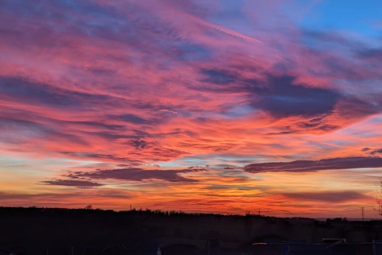 Shows various clouds towards the horizon lit in many shades of red and orange