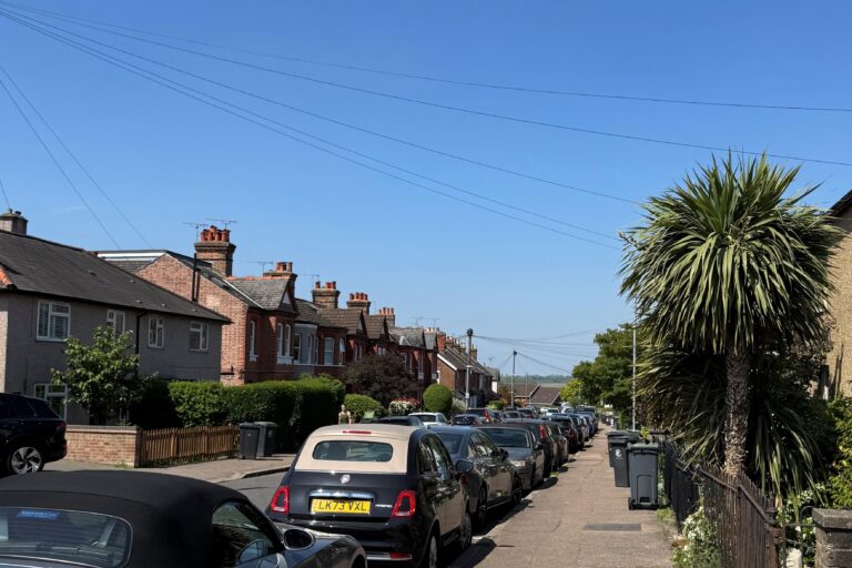 A suburban street with parked cars and a bright blue sky